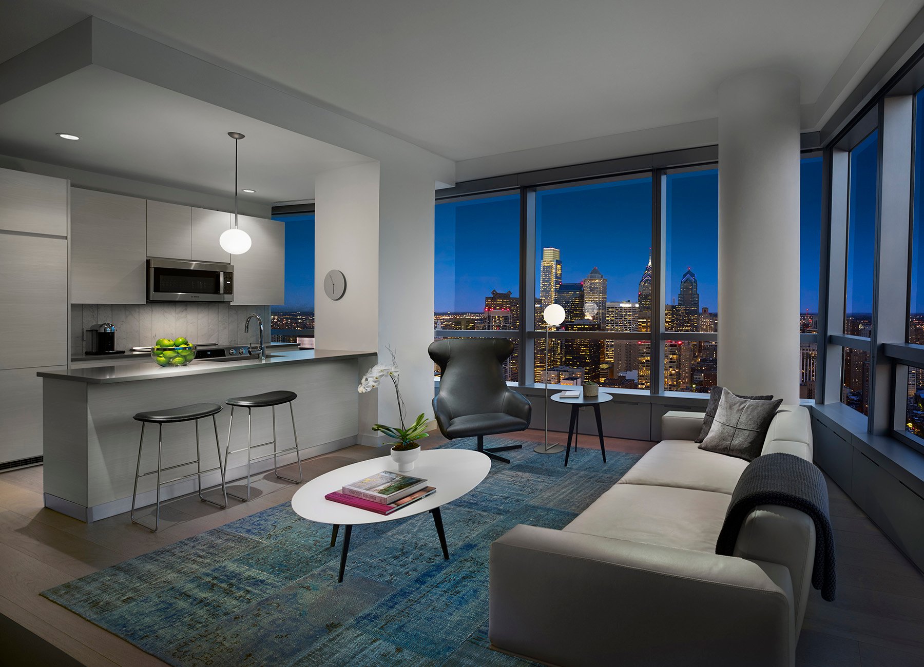 AKA University City living room with open kitchen and full-length window view of Philadelphia skyline at night 