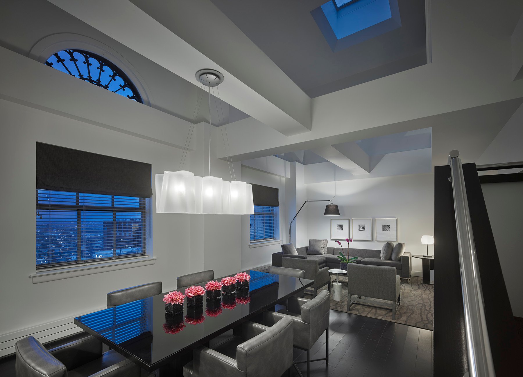 Philadelphia penthouse lounge with modern black and gray dining table for 8, stairs to second level, and arched windows showing dusk sky