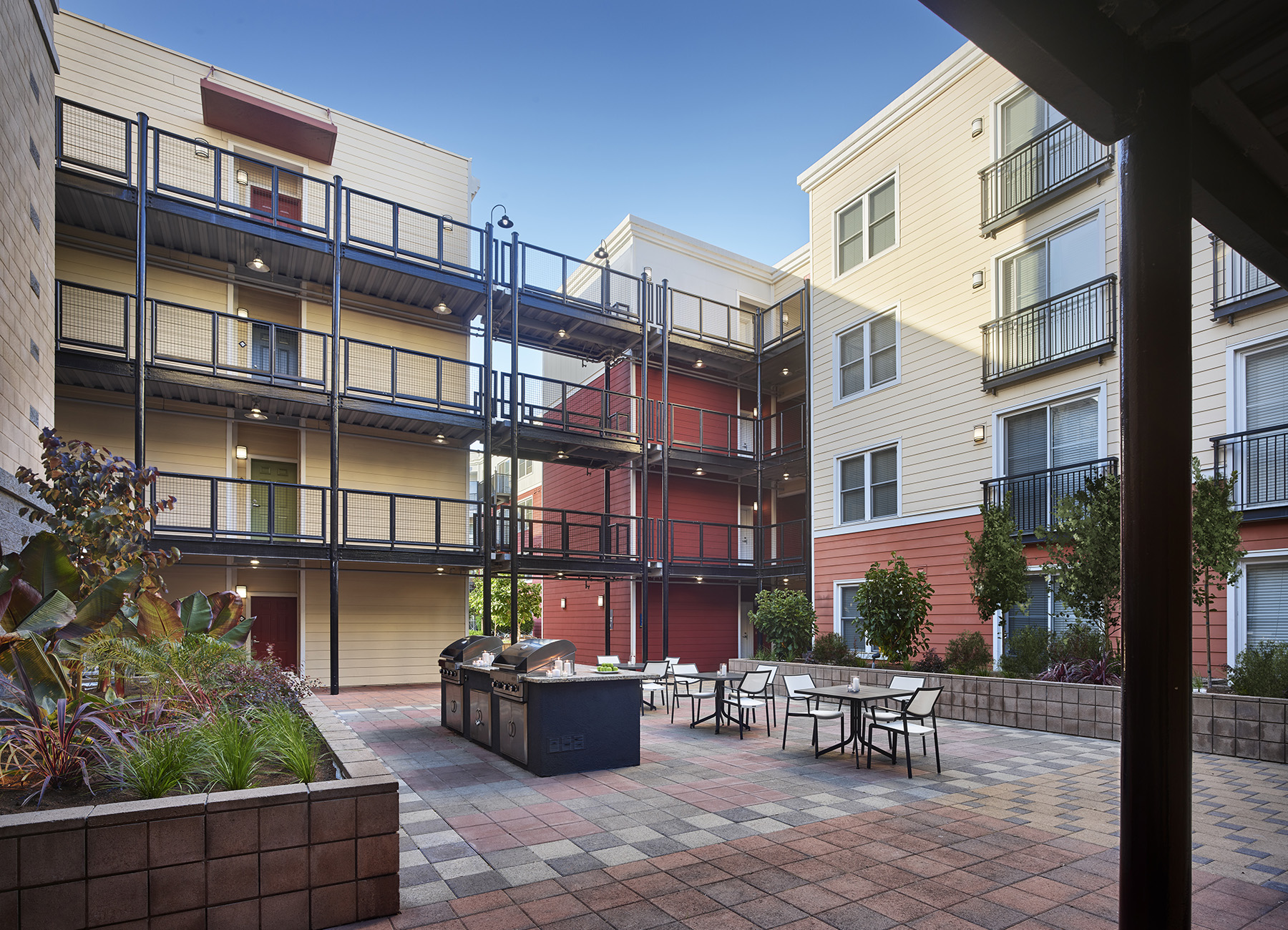 Exterior courtyard with tables and bbq grills, surrounded by a midrise AVE Emeryville apartment building
