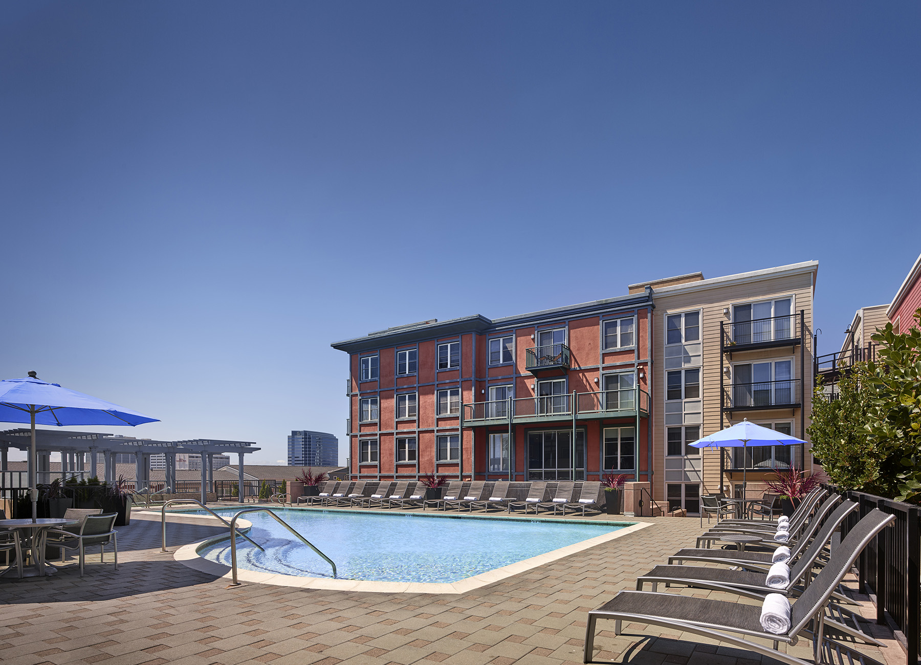 Large AVE Emeryville apartment courtyard with an in-ground pool and lounge chairs with blue umbrellas surrounding