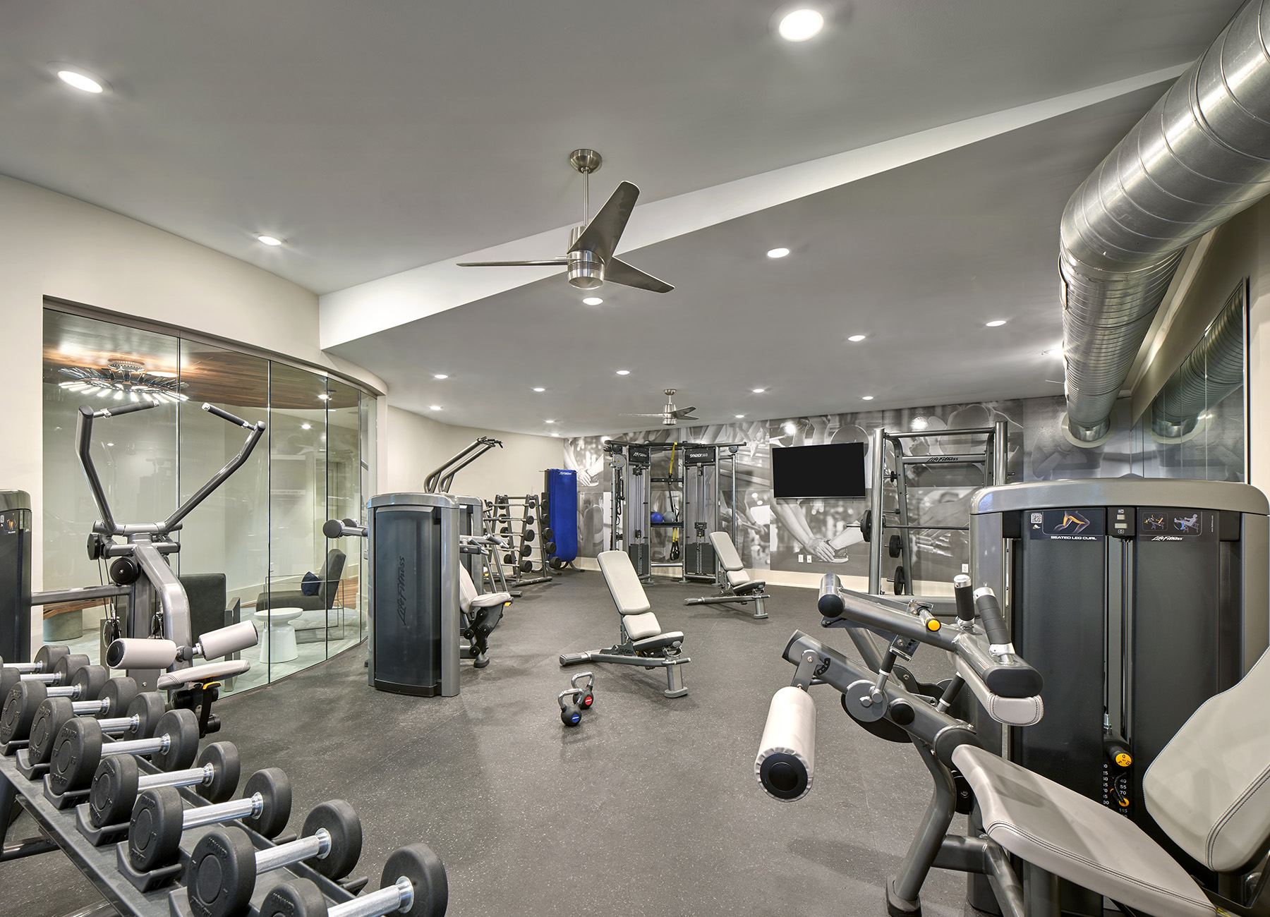 Modern fitness facility with cardio machines, free weights, and tvs