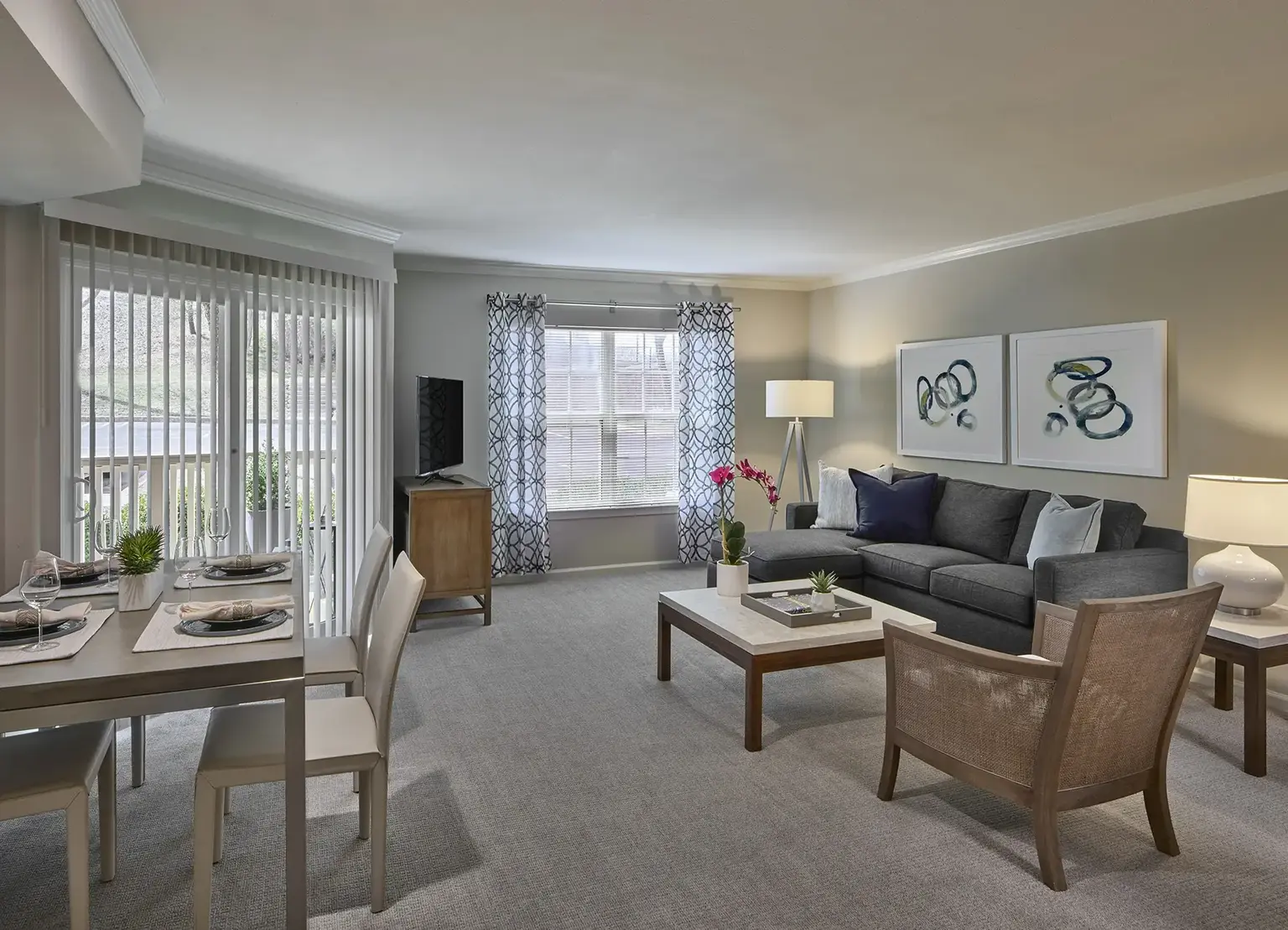 AVE Malvern furnished apartment living room with windows and light gray couch, tv, carpeted floors, and sliding glass door to balcony