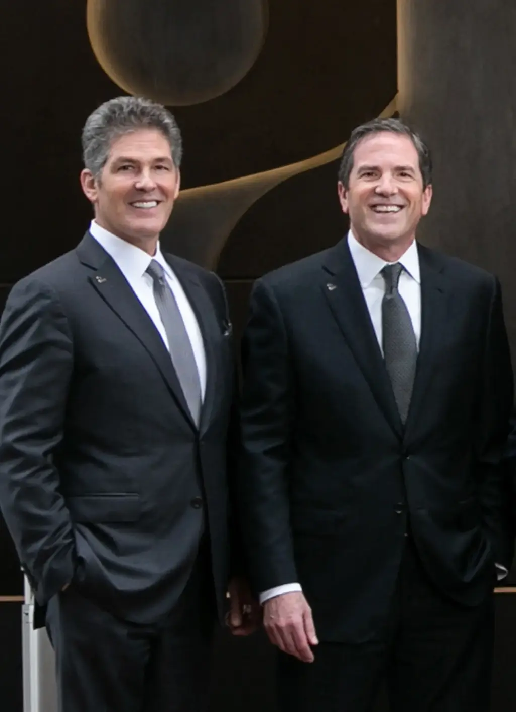 Larry and Brad Korman posing for a photo in front of an AKA sign