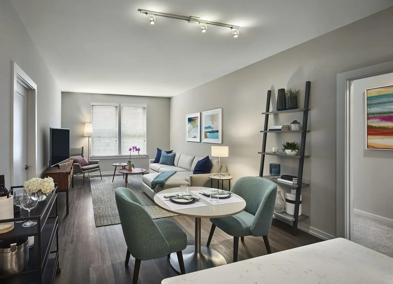 AVE King of Prussia apartment living room with blue cushions on gray couch and ladder shelf by bedroom door with round dining table in foreground